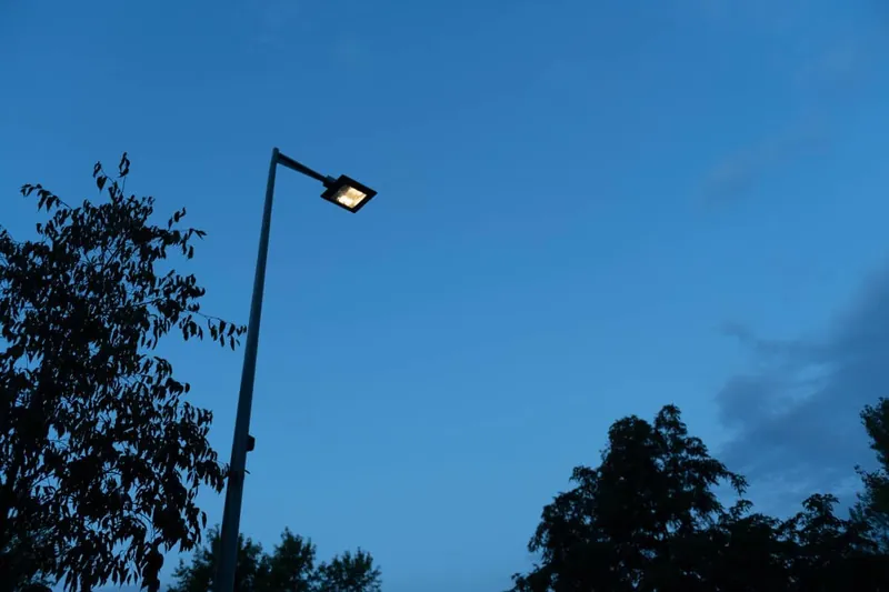 Luminaire LED sur mât au crépuscule, lumière dirigée vers le sol sous un ciel dégagé
