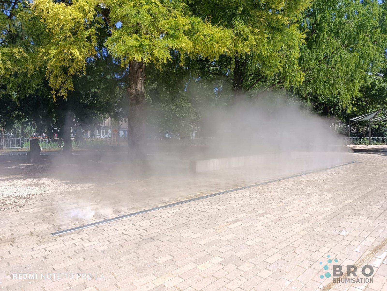 Nappe de brume BRO qui s'élève au ras d'une place pavée, sous les arbres, en plein été