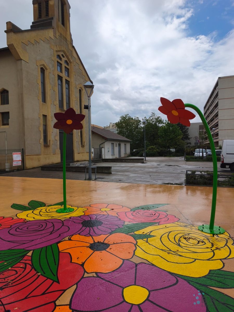 Brumisateurs BRO en forme de fleurs géantes sur un sol peint de fleurs colorées, devant une église