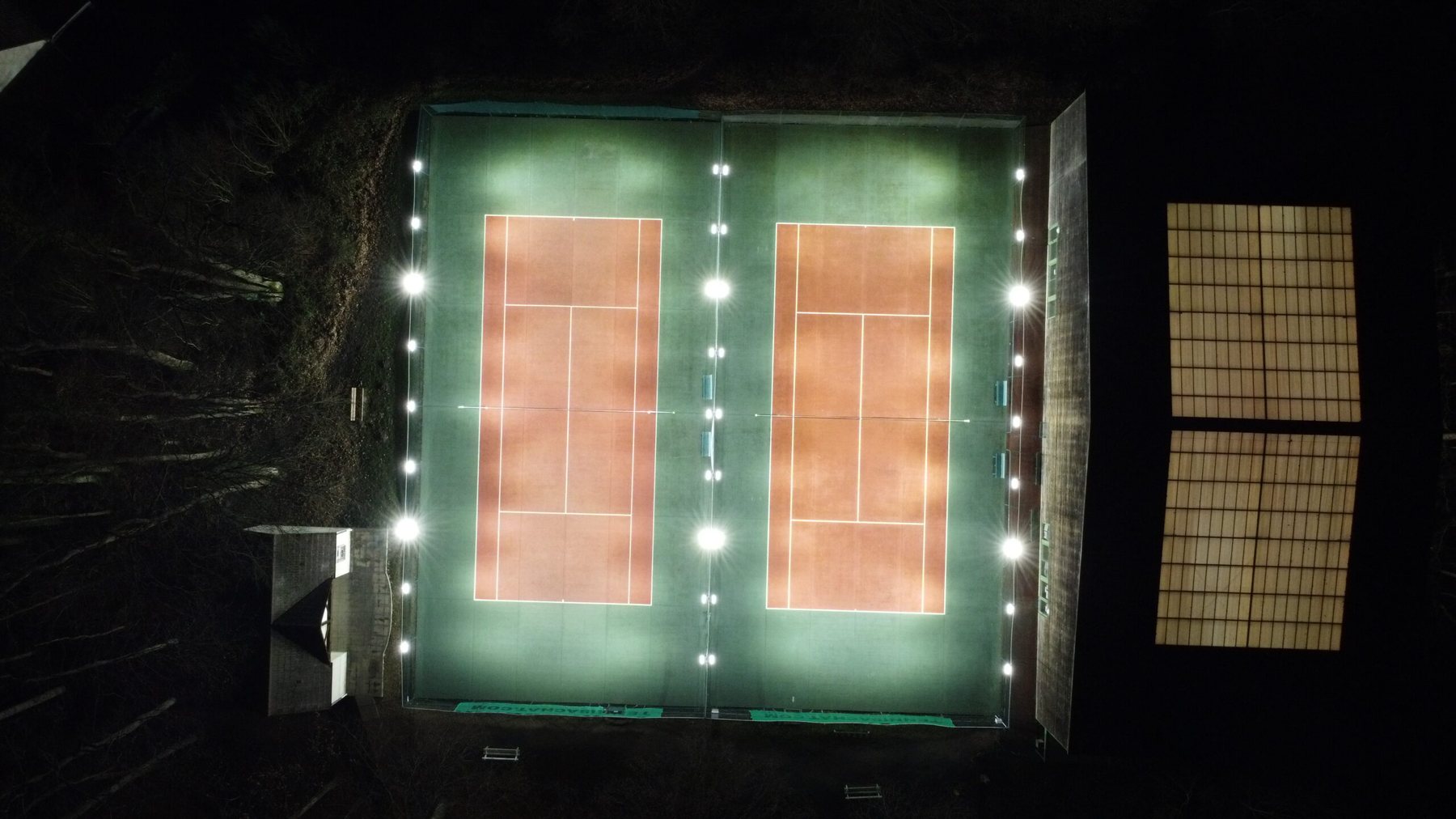Deux courts de tennis extérieurs éclairés de nuit par des kits LumiSET fixés sur le grillage, vue aérienne
