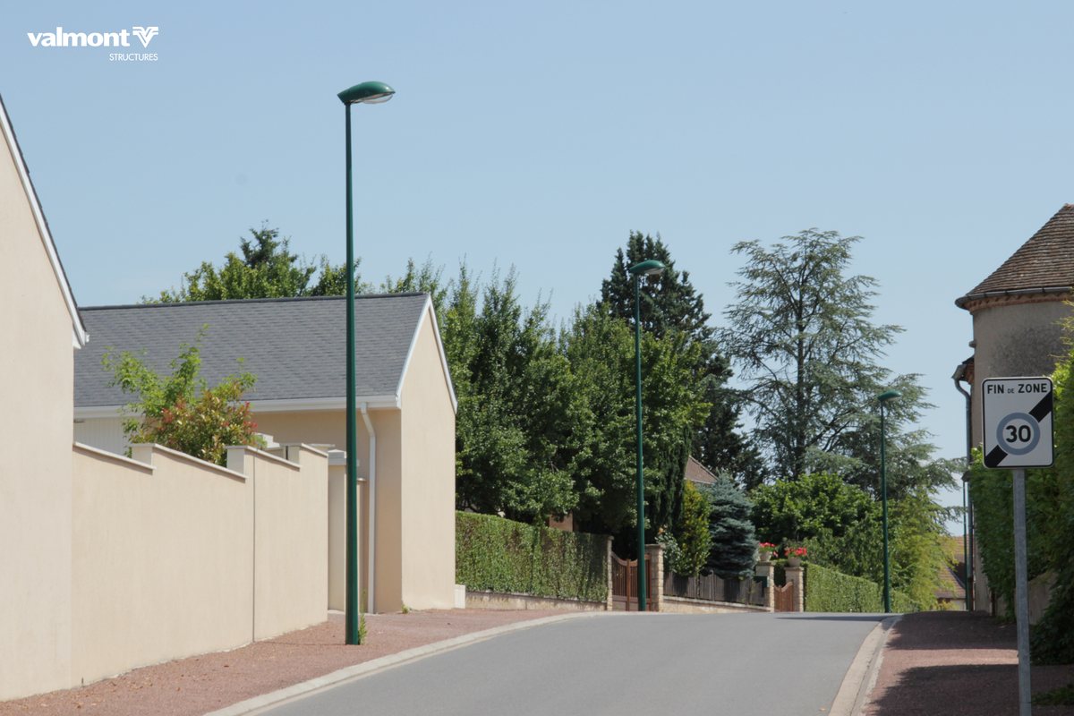 Mâts acier Saturne de Valmont, fûts verts avec luminaires en tête le long d'une rue résidentielle