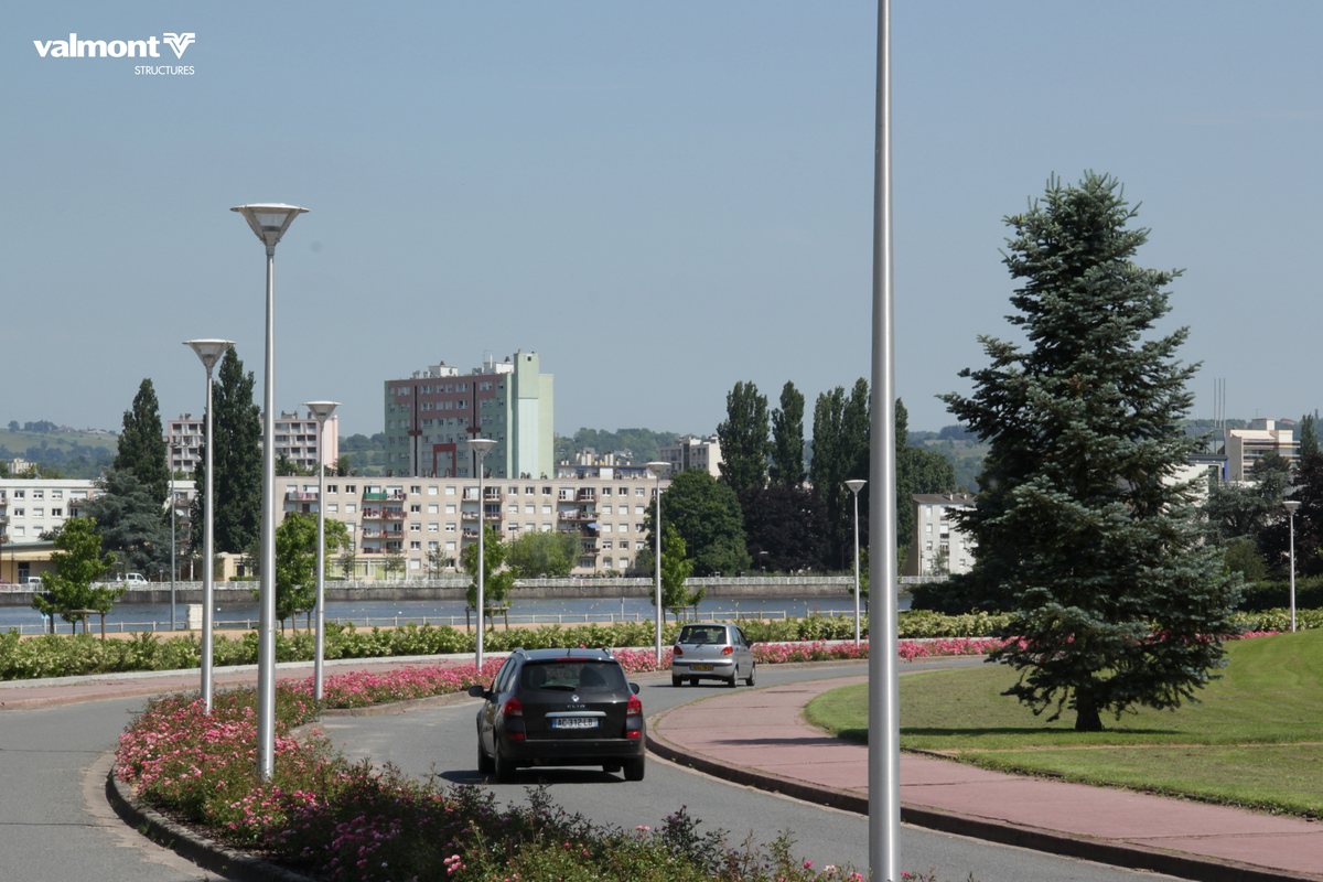 Mâts aluminium Vesta S de Valmont le long d'une avenue fleurie en bord de plan d'eau