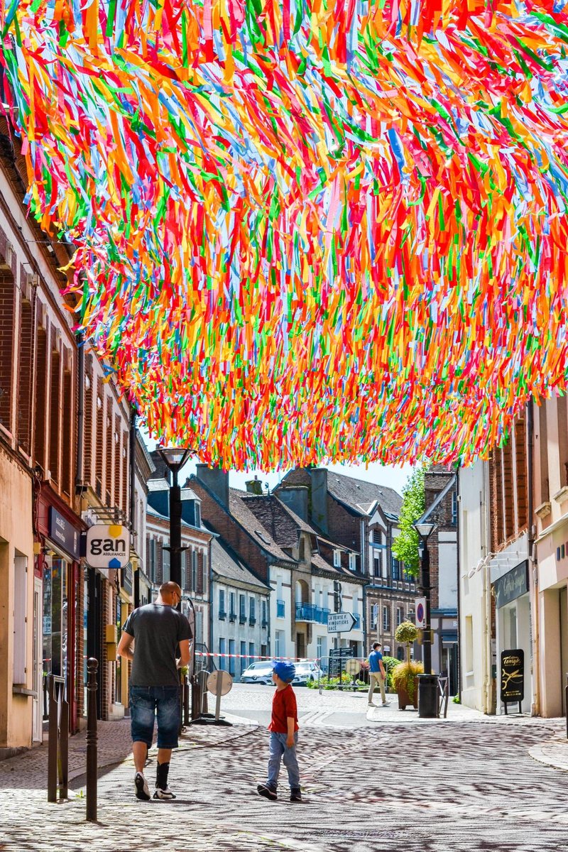Plafond climatique Ximénez : rubans multicolores tendus au-dessus d'une rue commerçante, un adulte et un enfant marchent à l'ombre